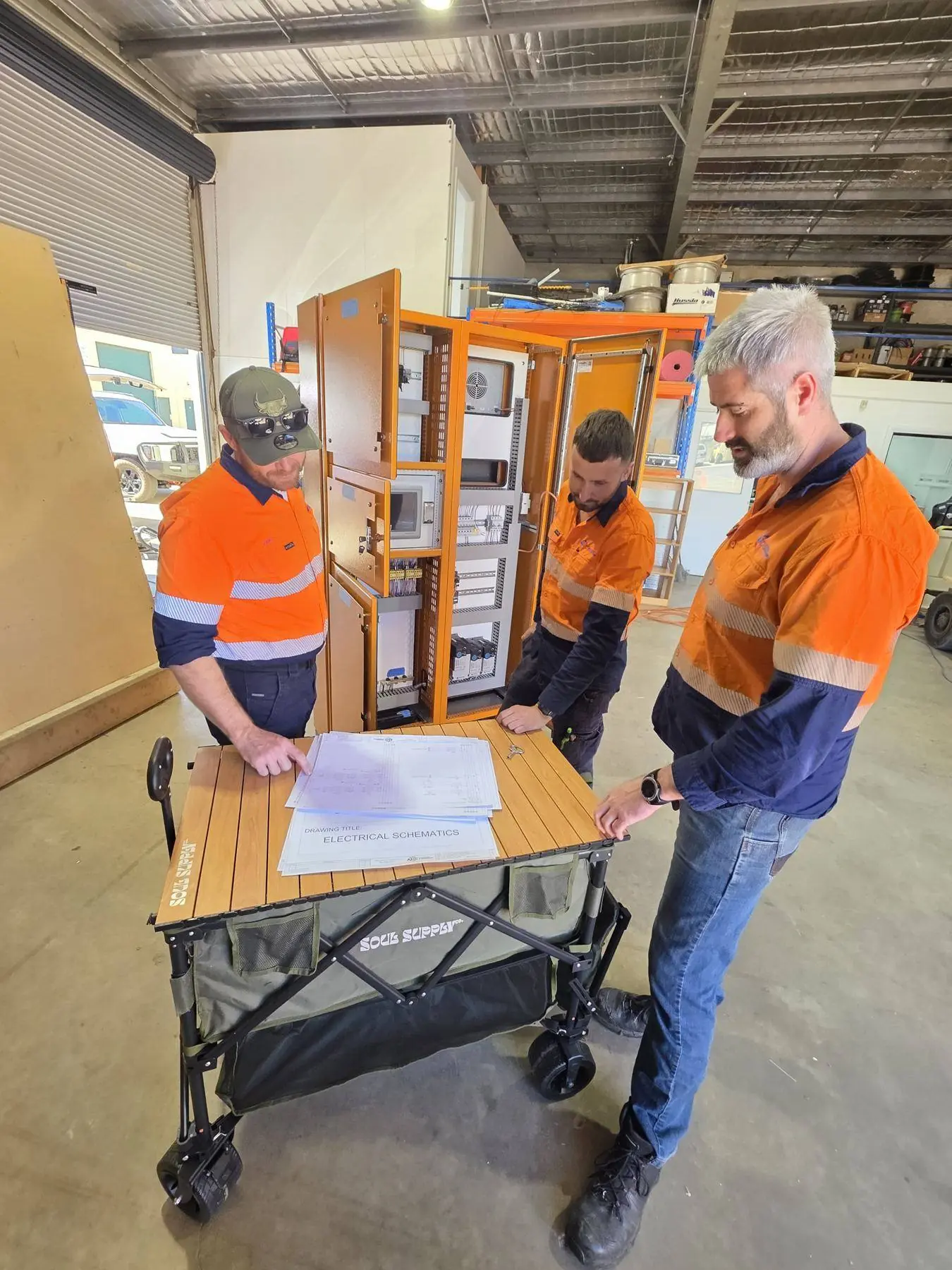 AMC engineers reviewing electrical schematics beside a control panel in the Griffith workshop